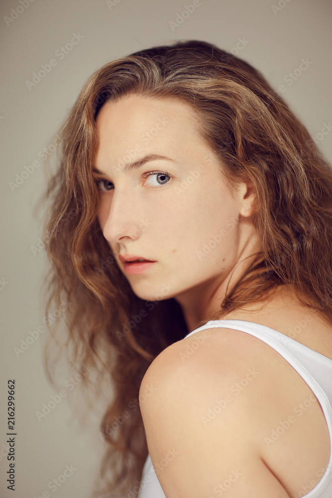 Naklejka premium Beautiful young woman with long curly hair and natural make up beauty portrait, looking into camera
