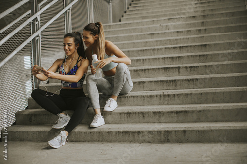 Two female runners looking on smart phone an rest after jogging