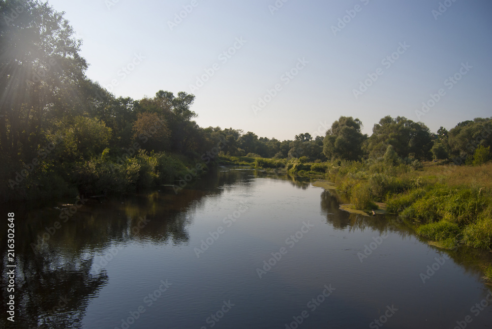 Landscape of the middle zone of Russia: the Nara River with low banks, overgrown with green grass and trees