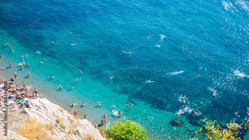 The top view and the beach. View from the high rocky shore. Azure-blue clear water. People swim in the beach. Black sea, Crimea