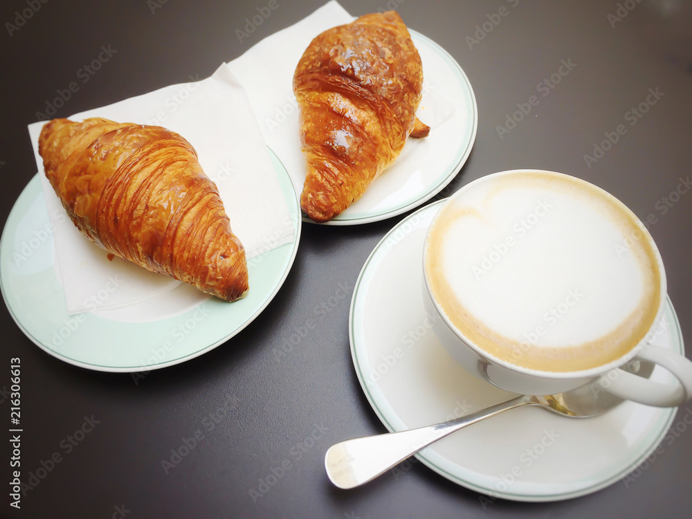 Tasty morning breakfast with a cup of foamy cappuccino and two fresh croissants