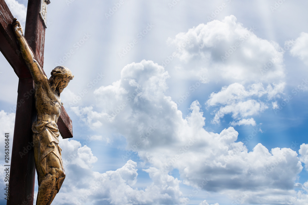 Jesus on a cross against blue sky with white clouds and rays of light ...