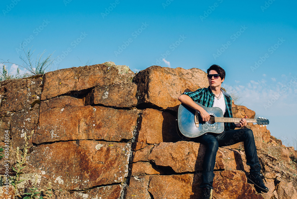 Fototapeta premium the guy plays guitar sitting big on the rocks