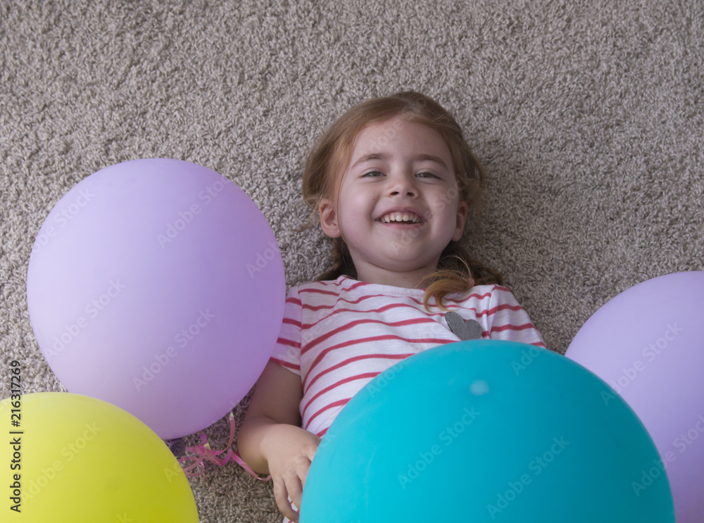 girl with balloons, child with balloons, child with balloons lying on floor. Girl is expressing creativity and looking at the camera and smiling. girl with balloons, child with balloons, child with balloons lying on floor. Girl is expressing creativity and looking at the camera and smiling.