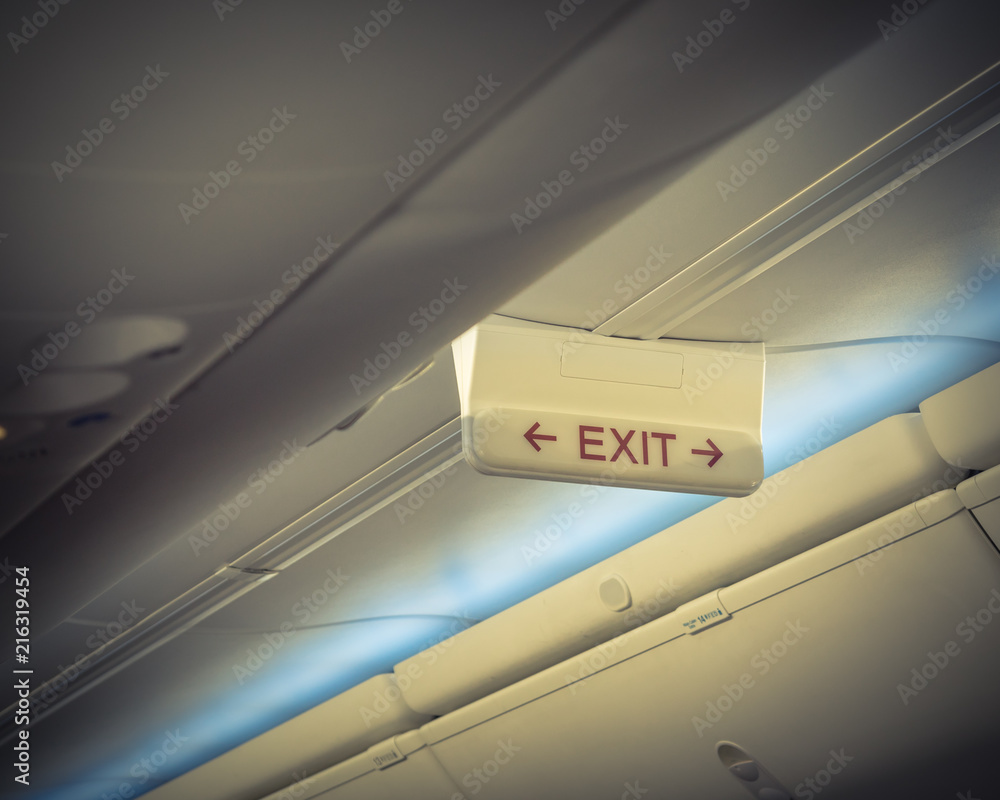 Emergency exit sign with red arrow on ceiling of airplane. Illuminated ...