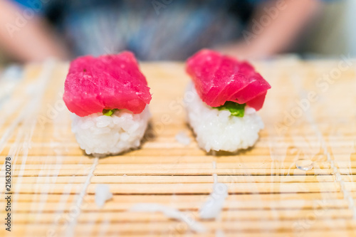 Macro closeup of nigiri tuna sushi on mat with plastic wrap and pink color