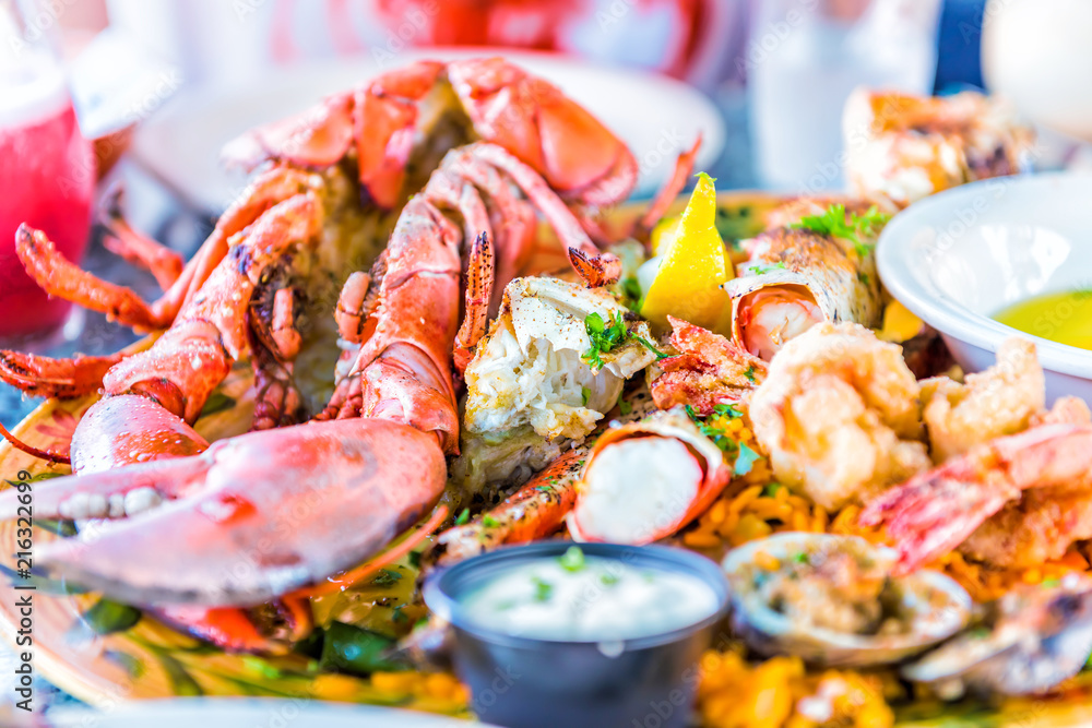 Macro closeup of whole lobsters in shell and seafood platter on plate with tartar sauce, garlic butter, shrimp tempura, crab meat, lemon, drinks, food Macro closeup of whole lobsters in shell and seafood platter on plate with tartar sauce, garlic butter, shrimp tempura, crab meat, lemon, drinks, food