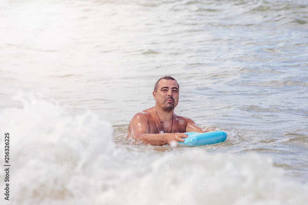 A large man bathes with an inflatable pillow in the seething sea.