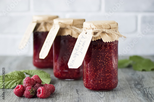 Bild auf Leinwand Homemade raspberry jam in glass jars on gray wooden table.