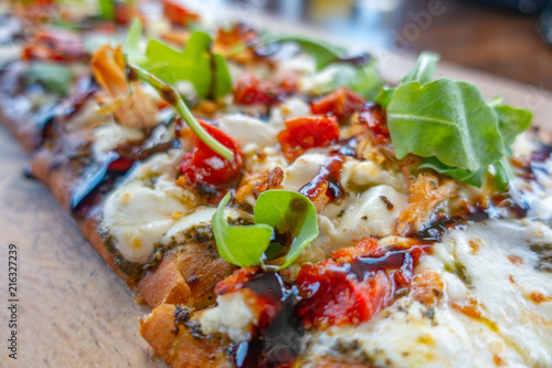 Chicken and Mozzarella Flatbread Pizza with herbs, tomatos and pesto sauce on wooden plate. Close up view .