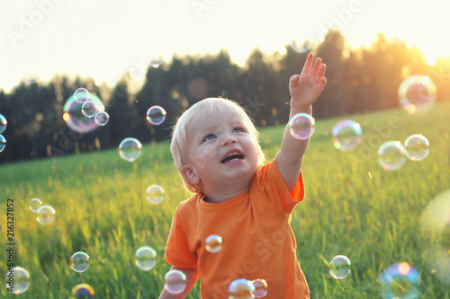 Foto Cute toddler blond boy playing with soap bubbles on summer field