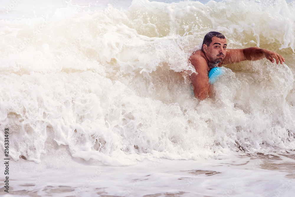 Fototapeta premium A man swims in the raging sea, it covers a huge wave.