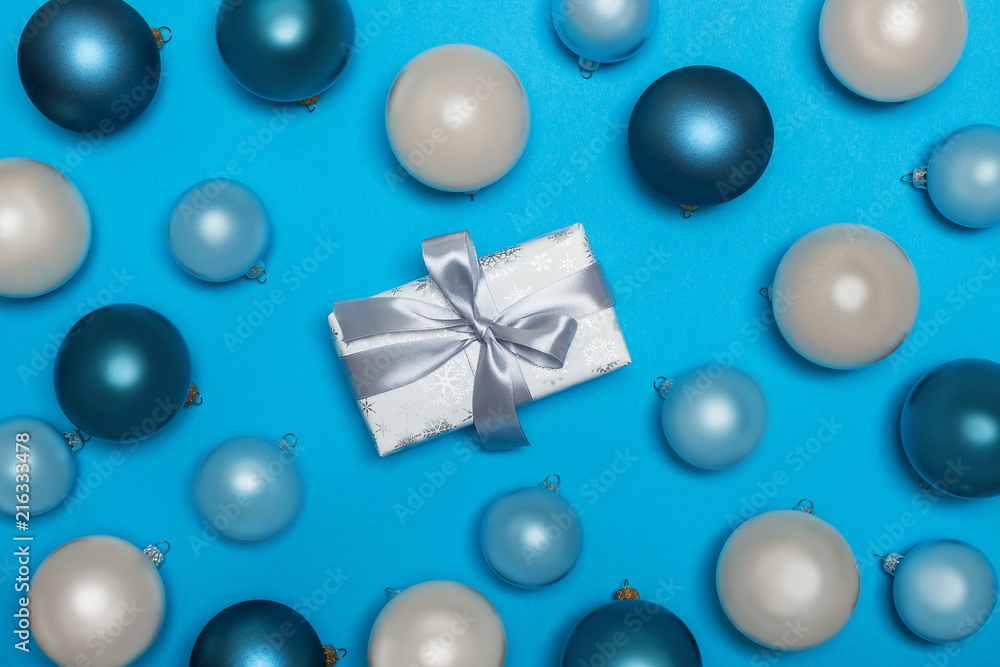 a view from above on New Year's and Christmas decorations, toys and a gift in a festive holiday paper with a bow. Gift and Christmas balls on a bright blue background. flat lay a view from above on New Year's and Christmas decorations, toys and a gift in a festive holiday paper with a bow. Gift and Christmas balls on a bright blue background. flat lay
