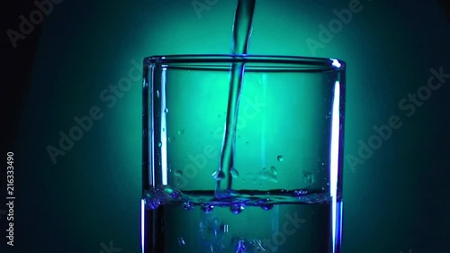 A glass of clear water on a bright background with a gradient fills to the brim in blue and green tones photo