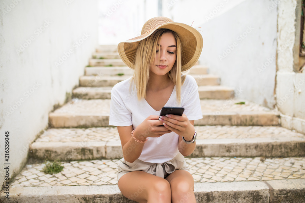 Young smiling woman sitting outdoors on stairs with smartphone, typing, surfing internet. Technology, education and remote working concept, copy space Young smiling woman sitting outdoors on stairs with smartphone, typing, surfing internet. Technology, education and remote working concept, copy space