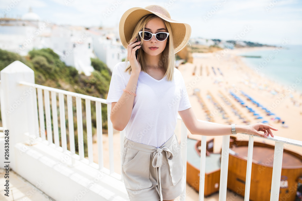 Happy woman talking on the phone while relaxing on outdoor on European vacation at seaside resort terrace hotel or at home.