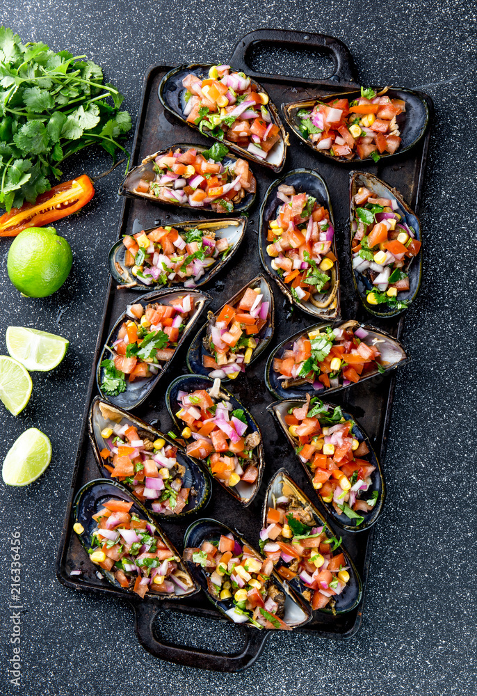 PERUVIAN FOOD. Choros a la chalaca. Big mussels, choros zapatos seasoned with purple onion, tomatoes, corn and lemon. Top view, black background. Traditional peruvian dish