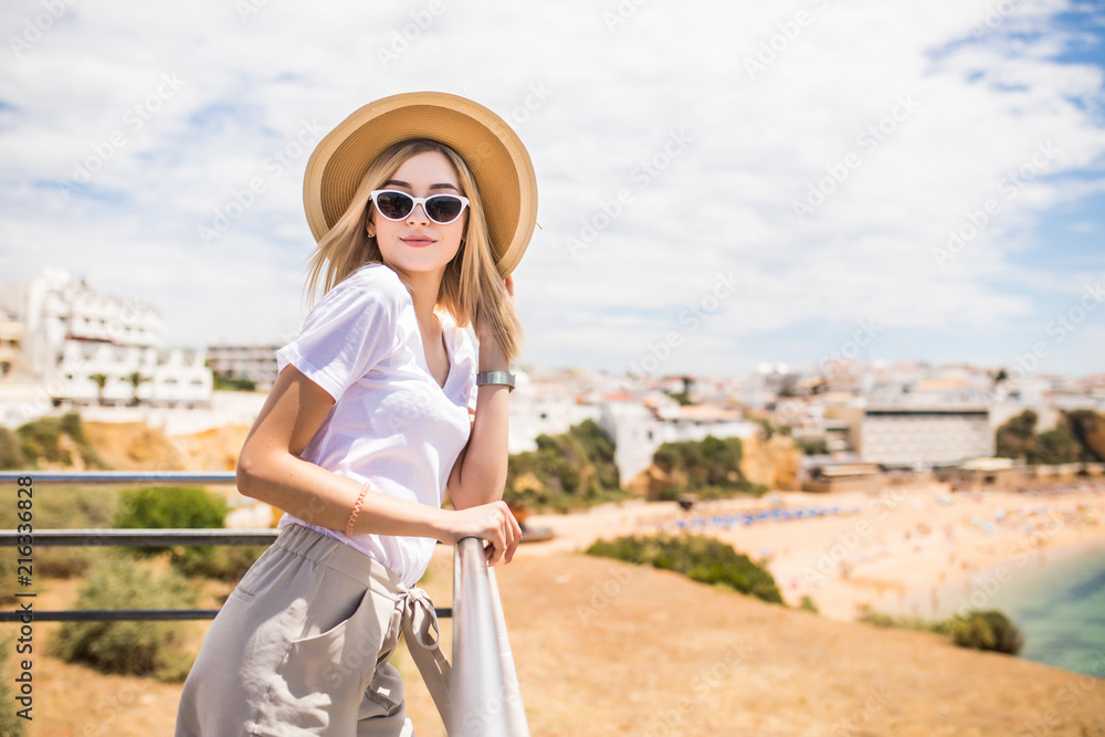 Fototapeta premium Portrait of young pretty woman with hat and sunglasses on the top near beach