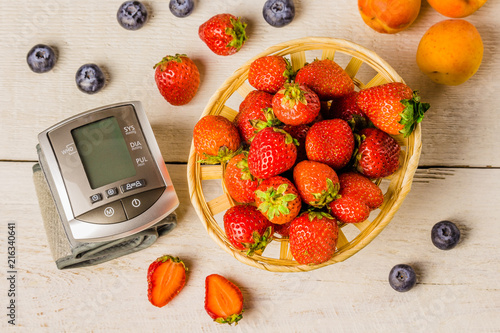 Tonometer, heart rate monitor to measure the body basket of strawberries on a white wooden vintage table blueberries and apricots. Desktop background. Food and drink top view