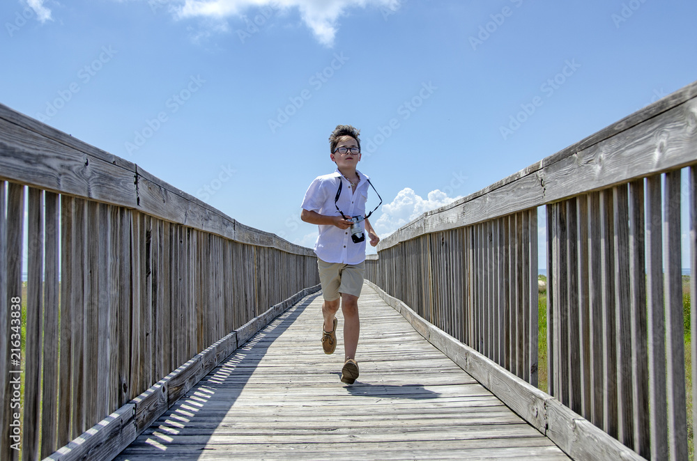 Young boy with camera running on boardwalk