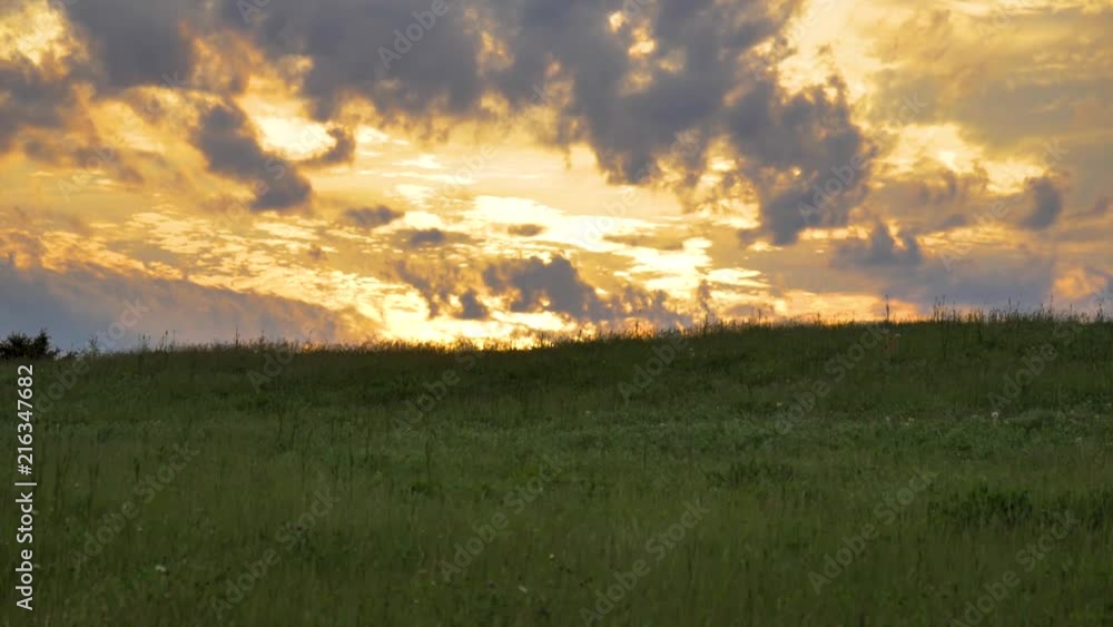 Incredibly dramatic sunset sky behind a hilltop over a field of green grass.