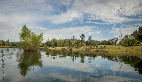 Fotografija Quiet, mountain lake with submerged tree and rocky bank, clouds reflected in wat