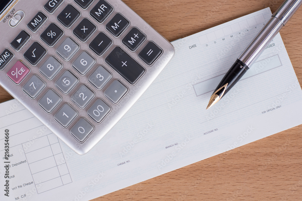 Mock up image of cheque book, pen and calculator on wooden background.