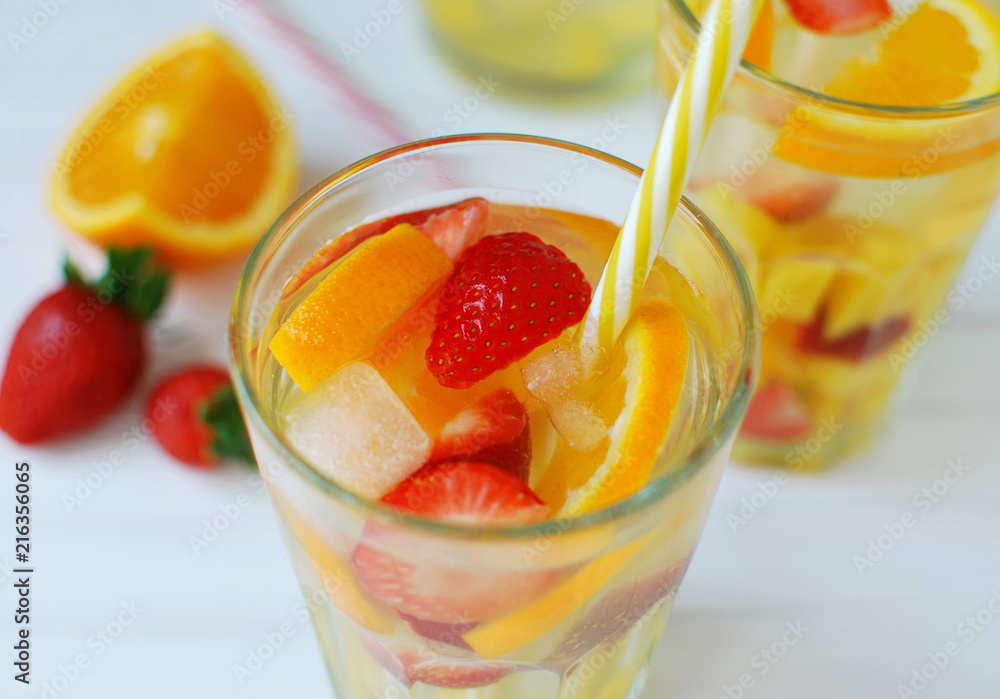 Refreshing summer drinks with strawberries and orange slices. Iced fruit drink in glass. Closeup view on white wooden background. Refreshing summer drinks with strawberries and orange slices. Iced fruit drink in glass. Closeup view on white wooden background.