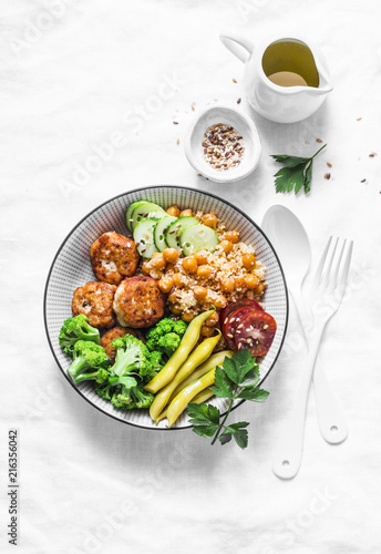 Healthy balanced buddha bowl lunch - spicy couscous with chickpeas, broccoli, green beans and turkey meatballs on light background, top view. Flat lay