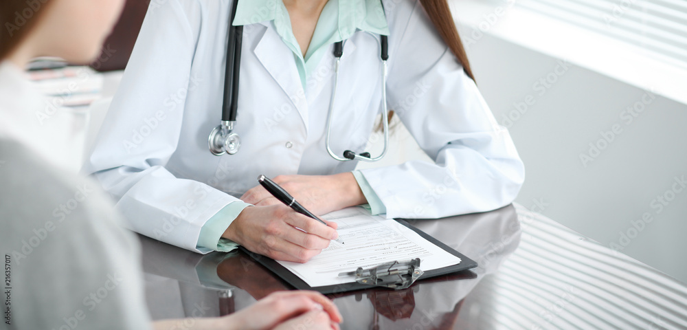 Doctor and patient in hospital. Physician filling up medication history records while talking with young woman. Healthcare and medicine concept Doctor and patient in hospital. Physician filling up medication history records while talking with young woman. Healthcare and medicine concept