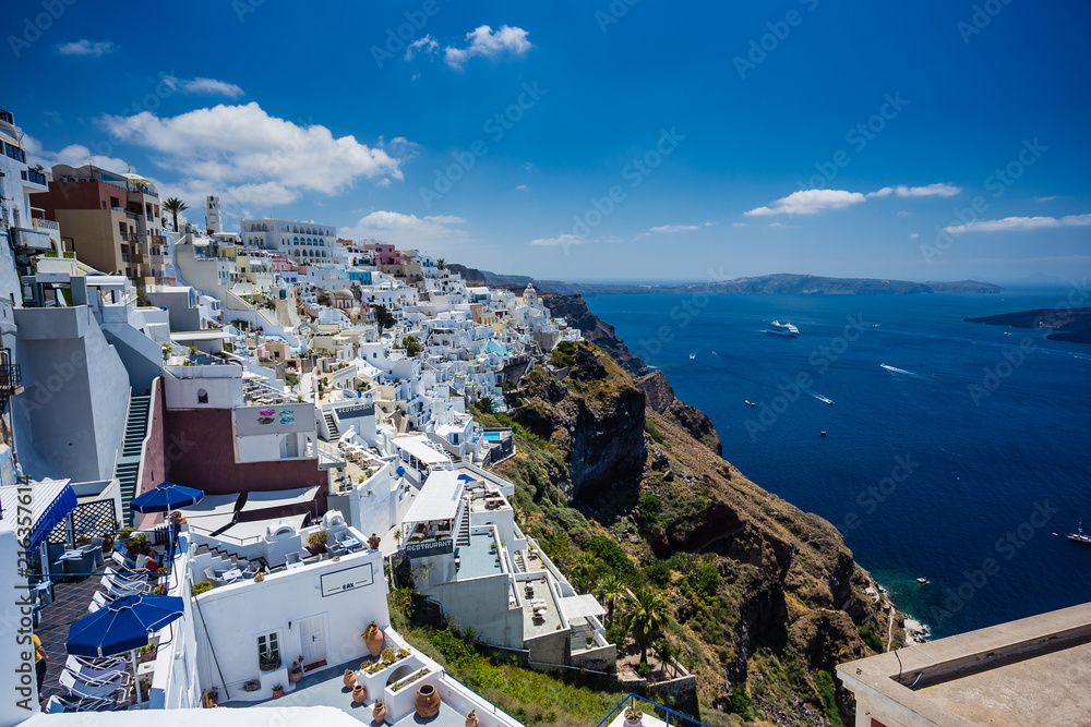 Obraz premium Przepiękny widok z otoczonego białymi murami miasta Fira na Santorini, Grecja, z oceanem, klifami i kalderą Santorini w tle.