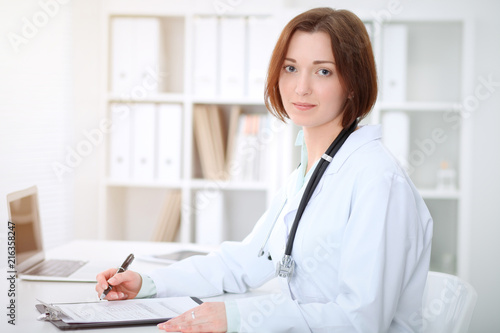 Young brunette female doctor sitting at the table and working at hospital office