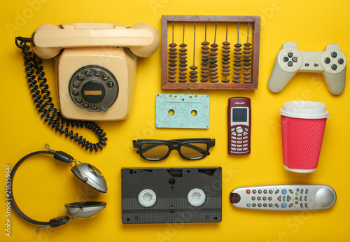 Retro objects on a yellow background. Rotary telephone, audio cassette, video cassette, gamepad, 3d glasses, tv remote, headphones, push-button phone. Analog media technology of the past. Flat lay.. photo