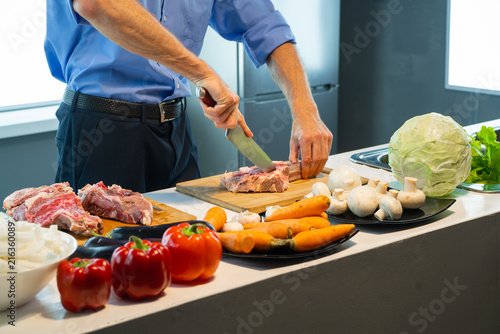A man in a blue shirt is cutting meat