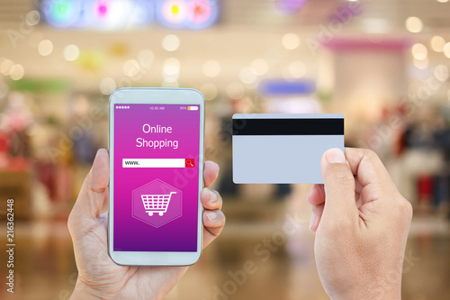 Hand holding smart phone with online shopping on screen and credit card over blurred in shopping mall background for mobile banking payment online concept