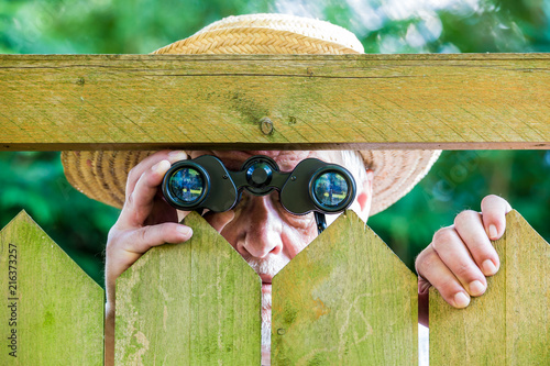 a curious neighbor stands behind a fence and watches with binoculars
