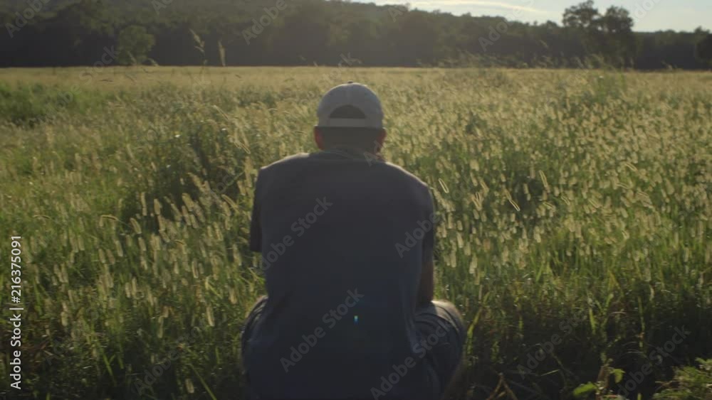 A photographer gazes ahead at the golden field in front of him as the camera pans to reveal his camera set up on a tripod waiting. A photographer gazes ahead at the golden field in front of him as the camera pans to reveal his camera set up on a tripod waiting.