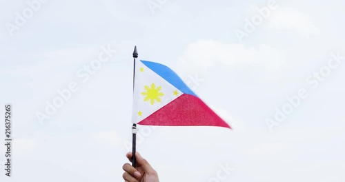 Hand raising Philippines national flag under clear sky with white clouds. Shot outdoors in 4k resolution photo