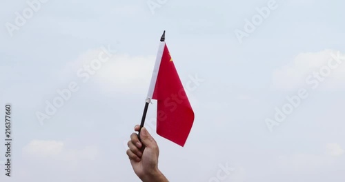 Hand waving national flag of China under clear sky with white clouds. Shot in 4k resolution photo