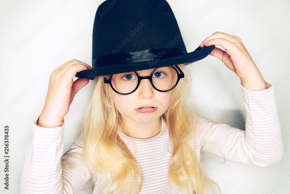 Little blonde girl wearing a hat and glasses looking sad