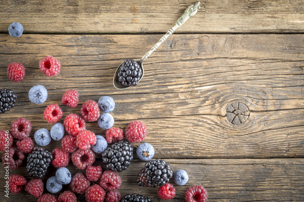 Freshly picked raspberries, blueberries and blackberries scattered on rustic old textured wooden table with silver spoon. Concept of healthy eating and nutrition for all family. Freshly picked raspberries, blueberries and blackberries scattered on rustic old textured wooden table with silver spoon. Concept of healthy eating and nutrition for all family.