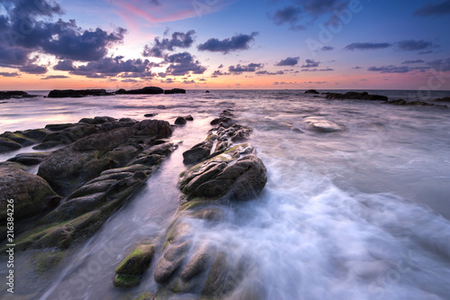 view of beautiful sunset at the beach with natural coastal rocks covered by green moss. soft focus due to slow shutter effect. © udoikel09