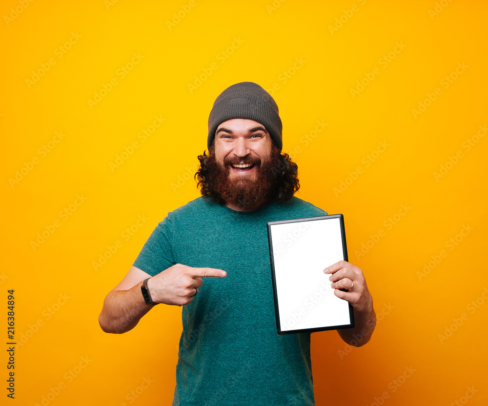 Young bearded hipster man smiling at the camera showing blank white sheet for your text copy space. Young bearded hipster man smiling at the camera showing blank white sheet for your text copy space.