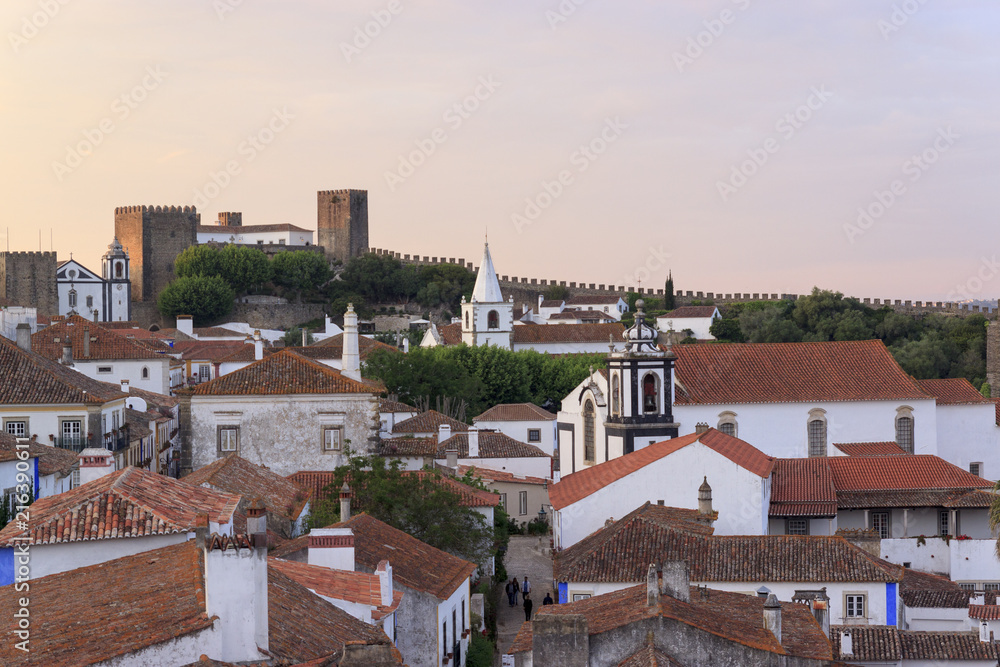 Scenic view of white houses red tiled roofs. and castle of Obidos from wall of fortress. Beautiful old town with medieval architecture in the sunset.