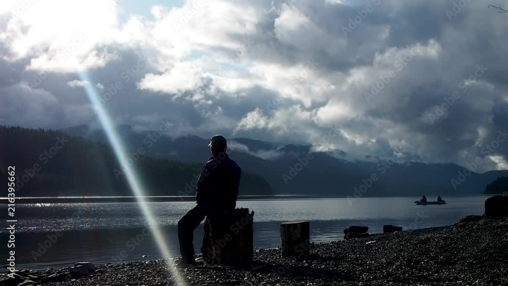 Man looking at canoe on a lake on a overcast day Man looking at canoe on a lake on a overcast day