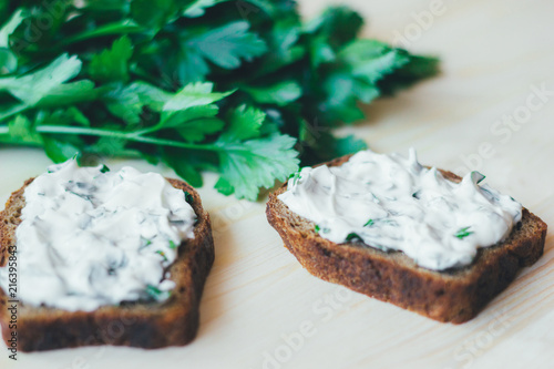 Toasts from greens and sour cream on a wooden background. Green branches of fresh parsley behind.