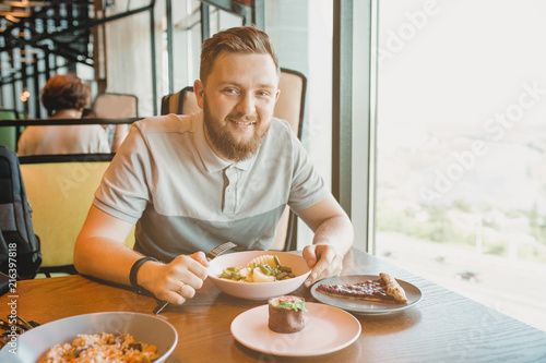 a man with a beard sitting at the table cafe and eating beans with potatoes, cakes next