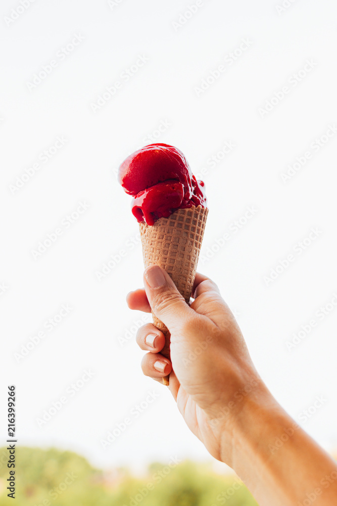 Woman's hand holding a refreshing and appetizing cone of raspberry ice cream, the ice cream slowly melts in the heat of summer Woman's hand holding a refreshing and appetizing cone of raspberry ice cream, the ice cream slowly melts in the heat of summer