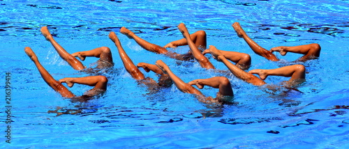 Synchronized Swimmers point up out of the water in action. Synchronized swimmers legs movement. Synchronized swimming team performing a synchronized routine of elaborate moves in the water.