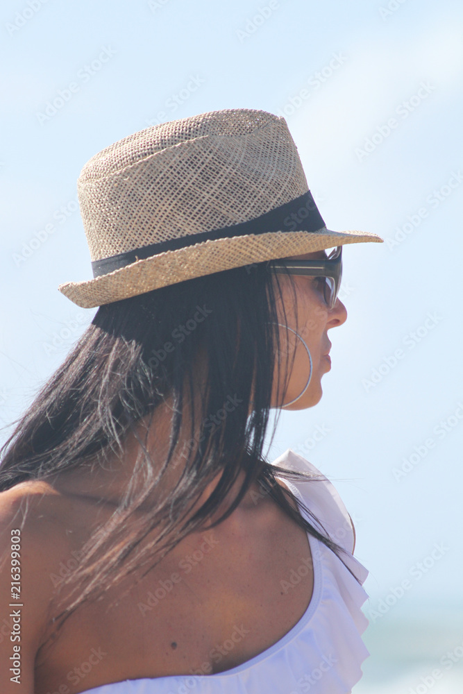 Beautiful woman with hat and white dress looking towards the horizon at the sea. Sabaudia, Lazio, Italy